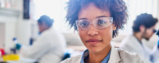 Portrait photo of young female African American researcher wearing a lab coat working in lab setting.